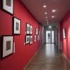 Framed photos on red gallery wall hung from paintable ArtiTeq primer Click Rail picture rail with clear perlon wires
