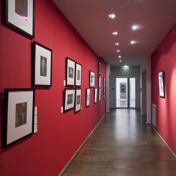 Framed photos on red gallery wall hung from paintable ArtiTeq primer Click Rail picture rail with clear perlon wires