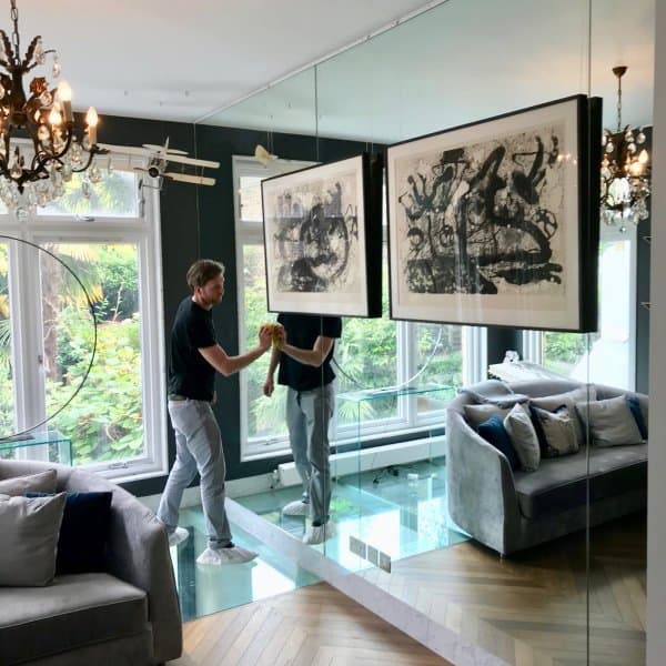 Man adjusts abstract prints hung on clear perlon wires from an ArtiTeq Click Rail picture rail fixed to a mirrored wall