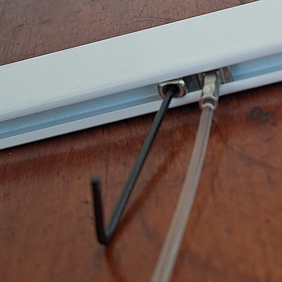 Tightening a sloped rail stopper Allen key tightening a sloped rail stopper inside a picture rail channel next to a hanging wire.