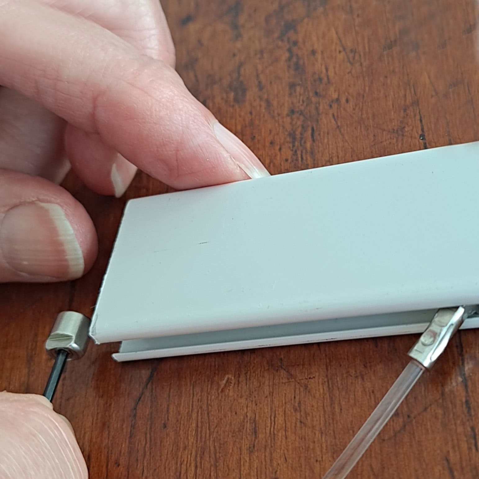 Sliding the stopper in from the rail end Hand sliding a sloped rail stopper into the end of a picture rail before positioning it under a hanging wire.