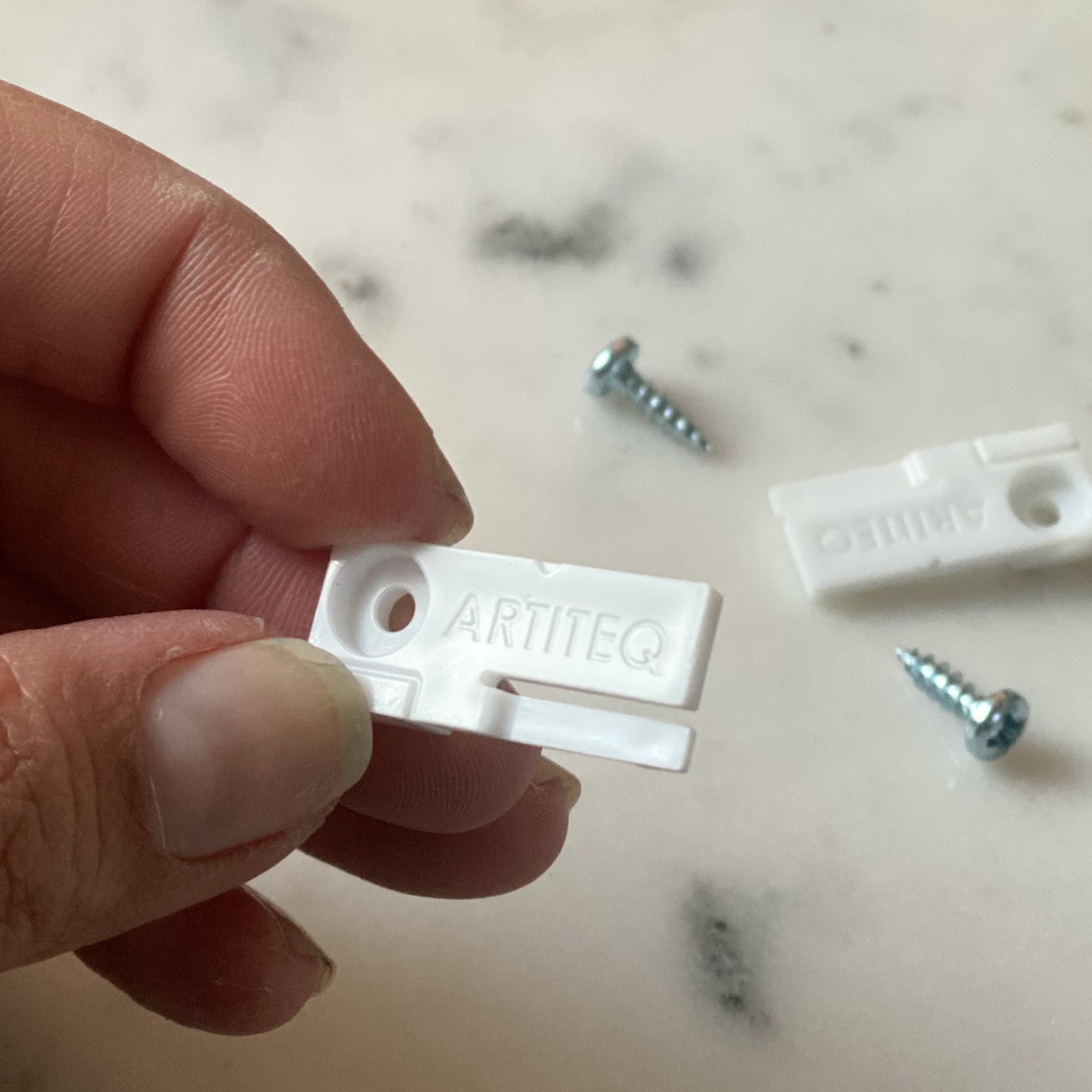 ArtiTeq Tilt Reducer Close-up Close-up photo of a white ArtiTeq tilt reducer held between fingers, with screws and a second reducer blurred in the background.