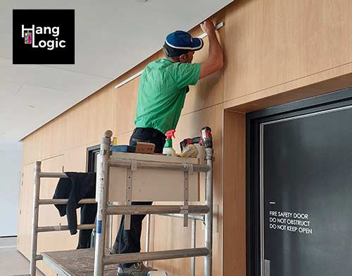 Hang Logic technician installing a picture rail using an Artiteq system on a wooden wall at ECH Encore Apartments.