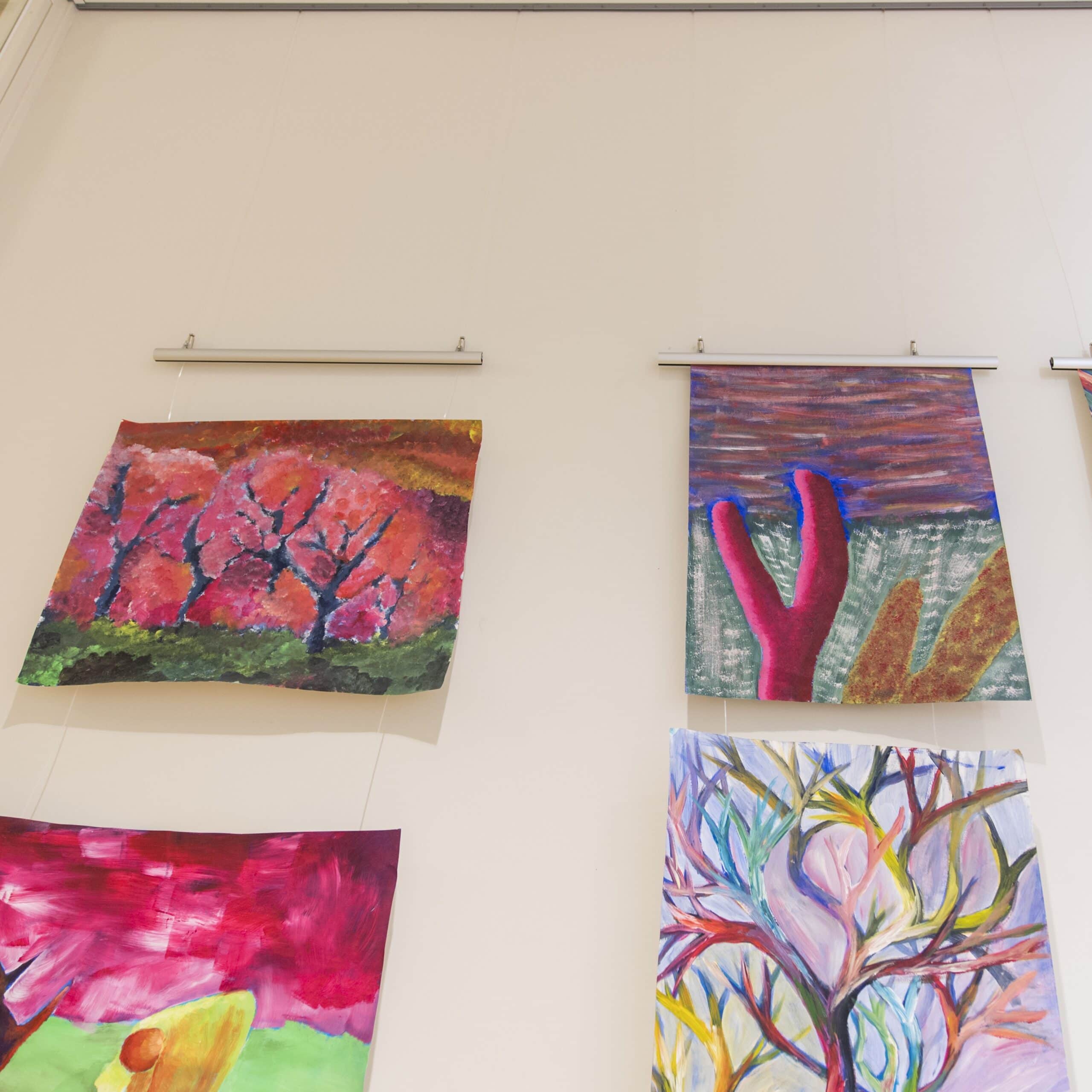 Multiple colourful paintings hang on a white wall using slim aluminium poster snap strips, showing an easy way to display and change artwork without frames.