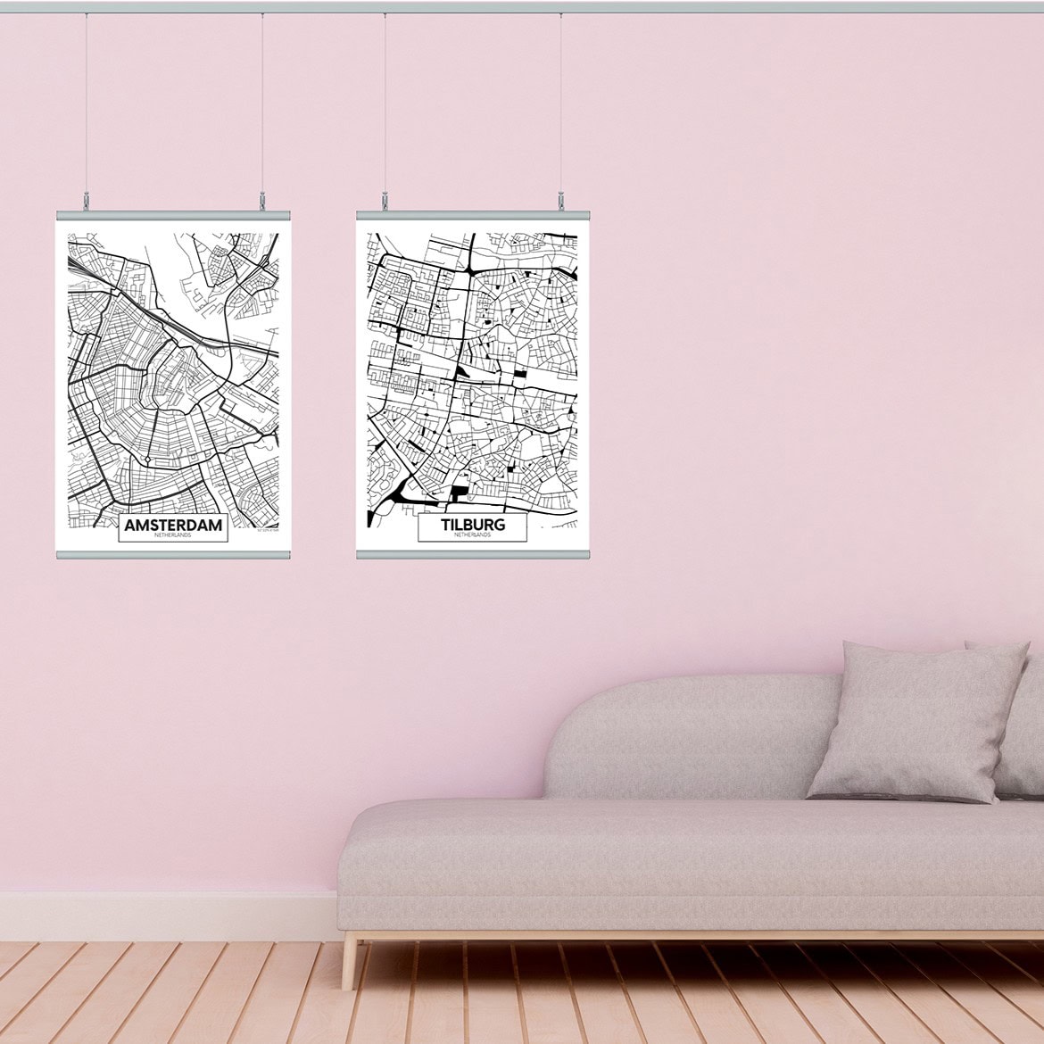 Two black-and-white city map posters labelled Amsterdam and Tilburg hang side by side on a pink wall using slim aluminium poster snap strips and thin suspension wires.