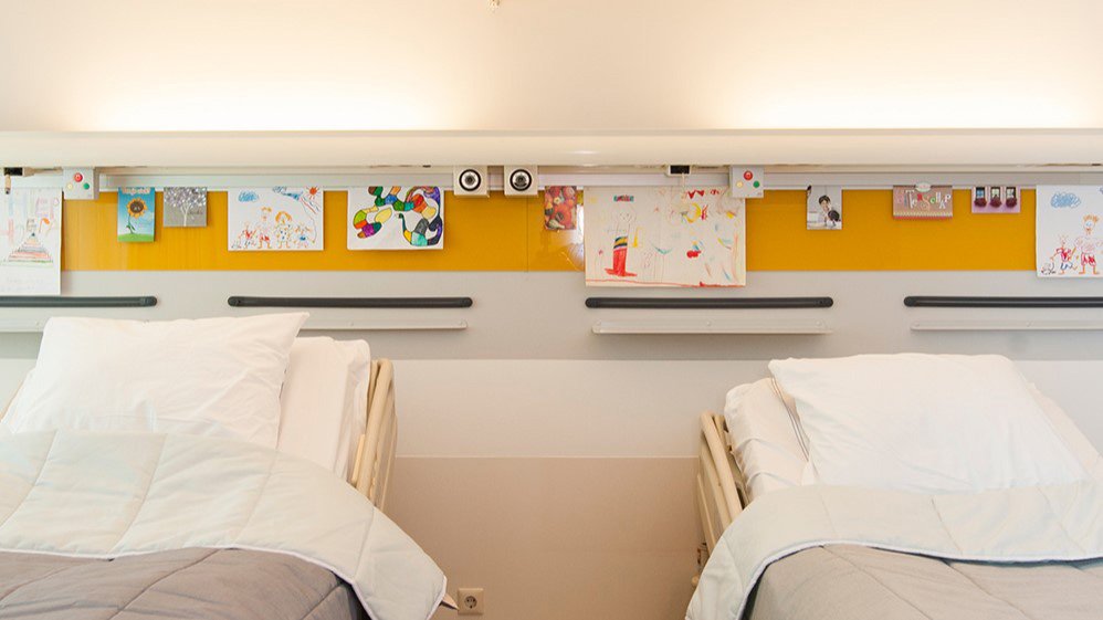 ArtiTeq Info Rail installed above two hospital beds, displaying children’s drawings and cards to create a personalized and uplifting environment. Available at Hang Logic.