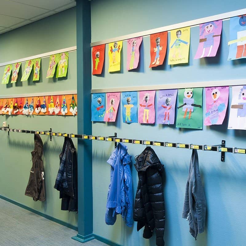 Artiteq Info Rail displaying colorful student artwork in a school hallway with coat hooks below.