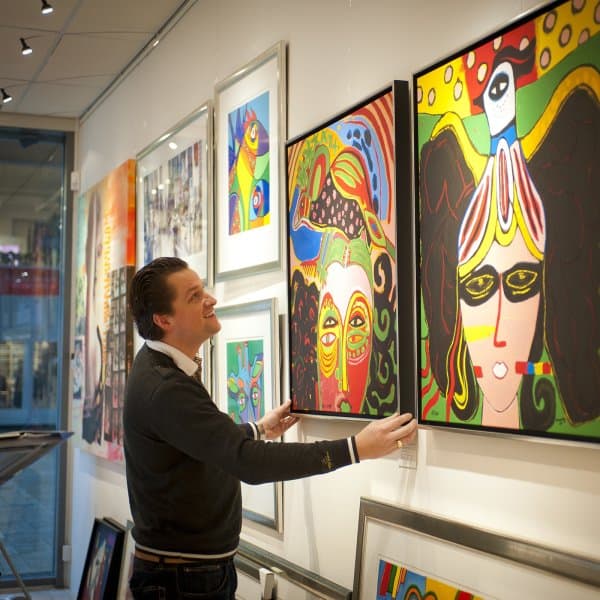 Gallery owner adjusting colourful canvases hung from Combi Rail PRO Light with integrated LED spots