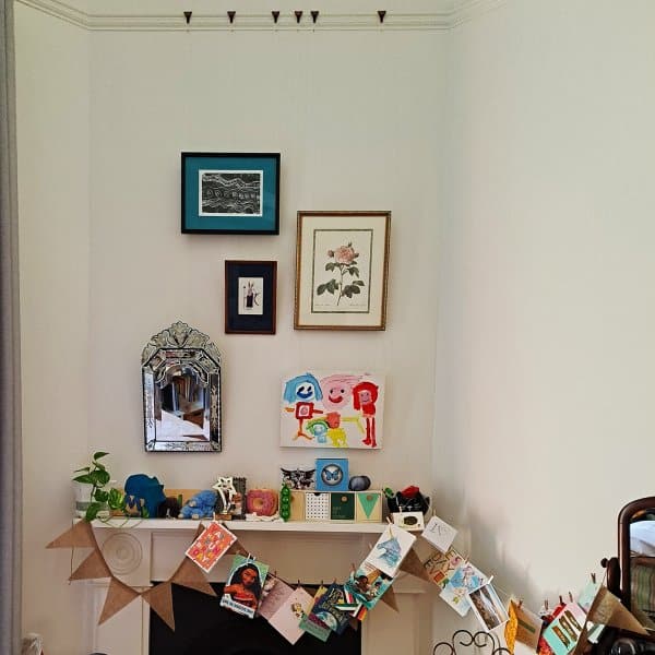 Living‑room fireplace with framed pictures hung on clear Perlon + Loop hanging wires from a timber picture rail.