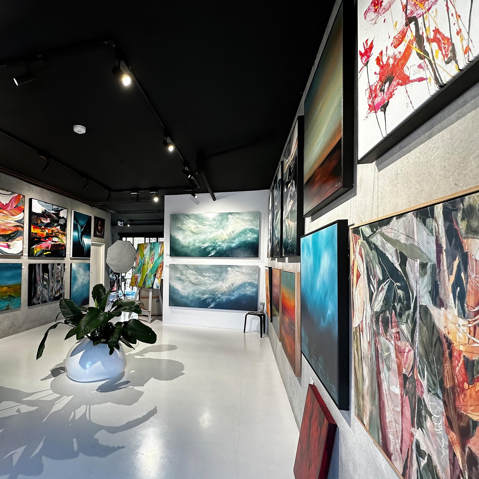 Contemporary gallery with black ceiling; dozens of canvases hung on clear wires from ArtiTeq Top Rail picture rail