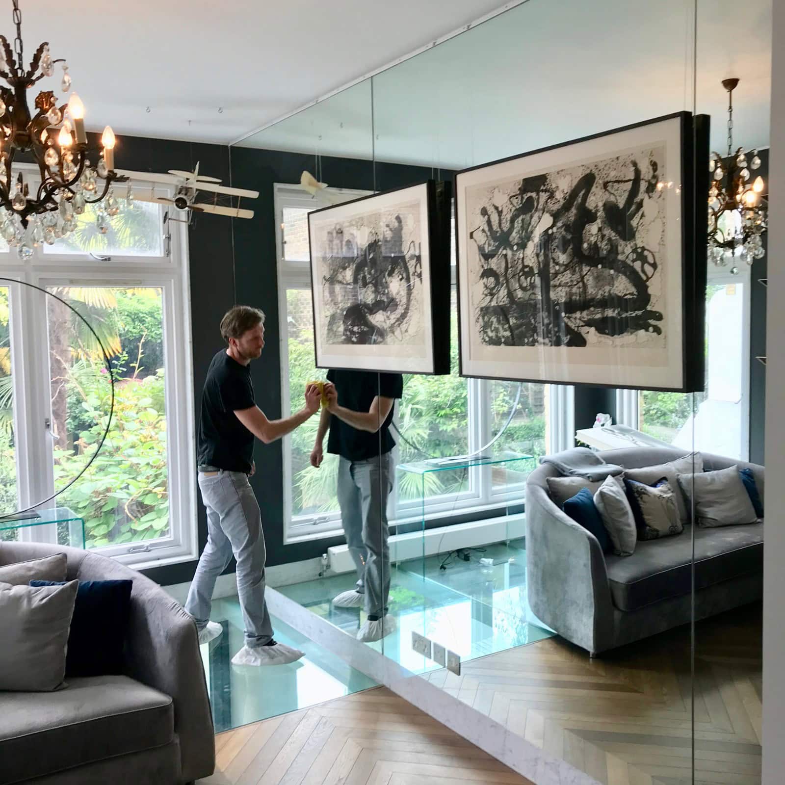 A professional installer hanging framed black-and-white art over a floor-to-ceiling mirrored wall using a rail system to avoid drilling into glass.