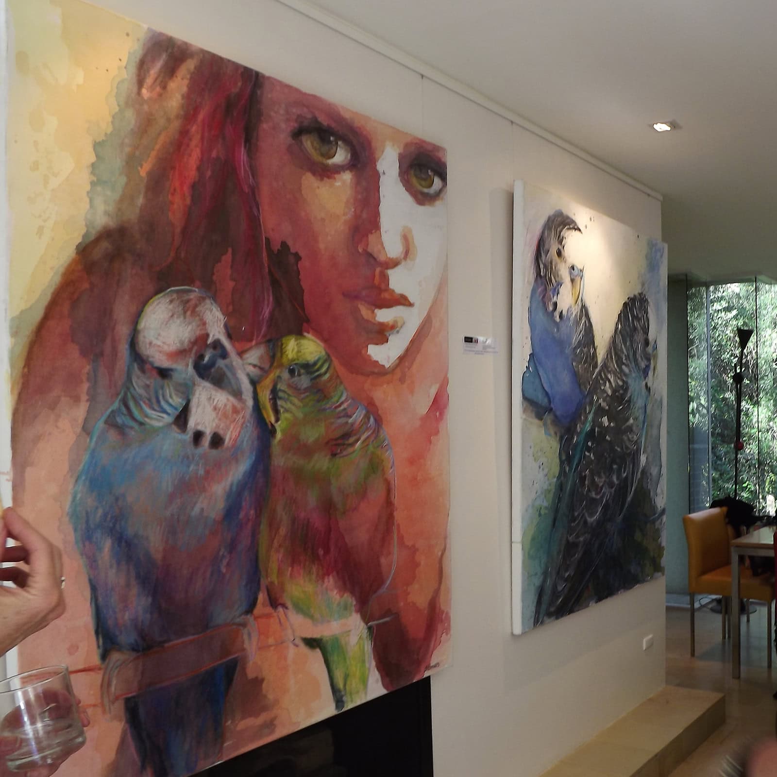 Large framed watercolor paintings of birds and portraits suspended by transparent perlon cords on an Artiteq gallery display system.