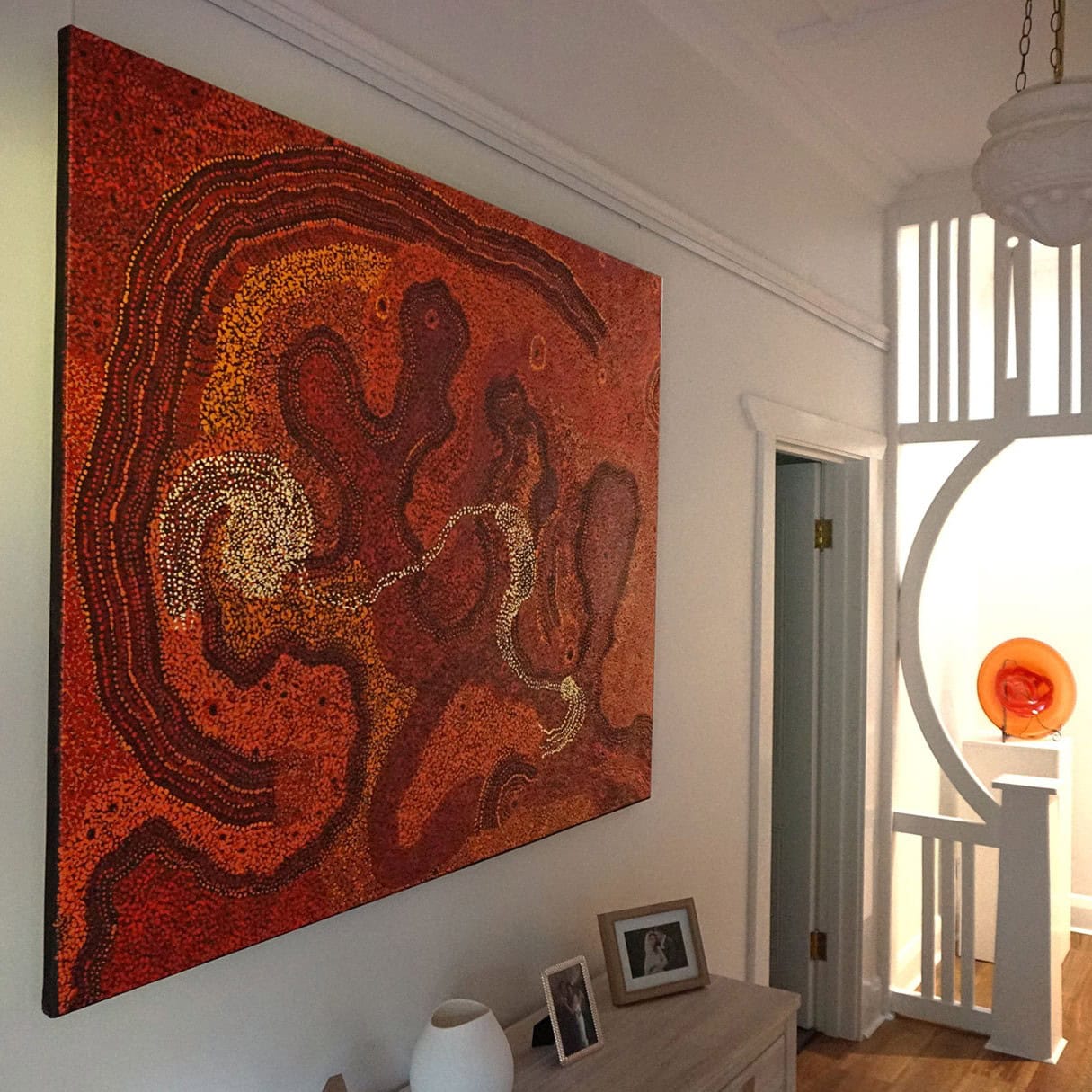 Large red Aboriginal dot painting hanging securely in a white hallway using the discreet ArtiTeq Click Rail system.