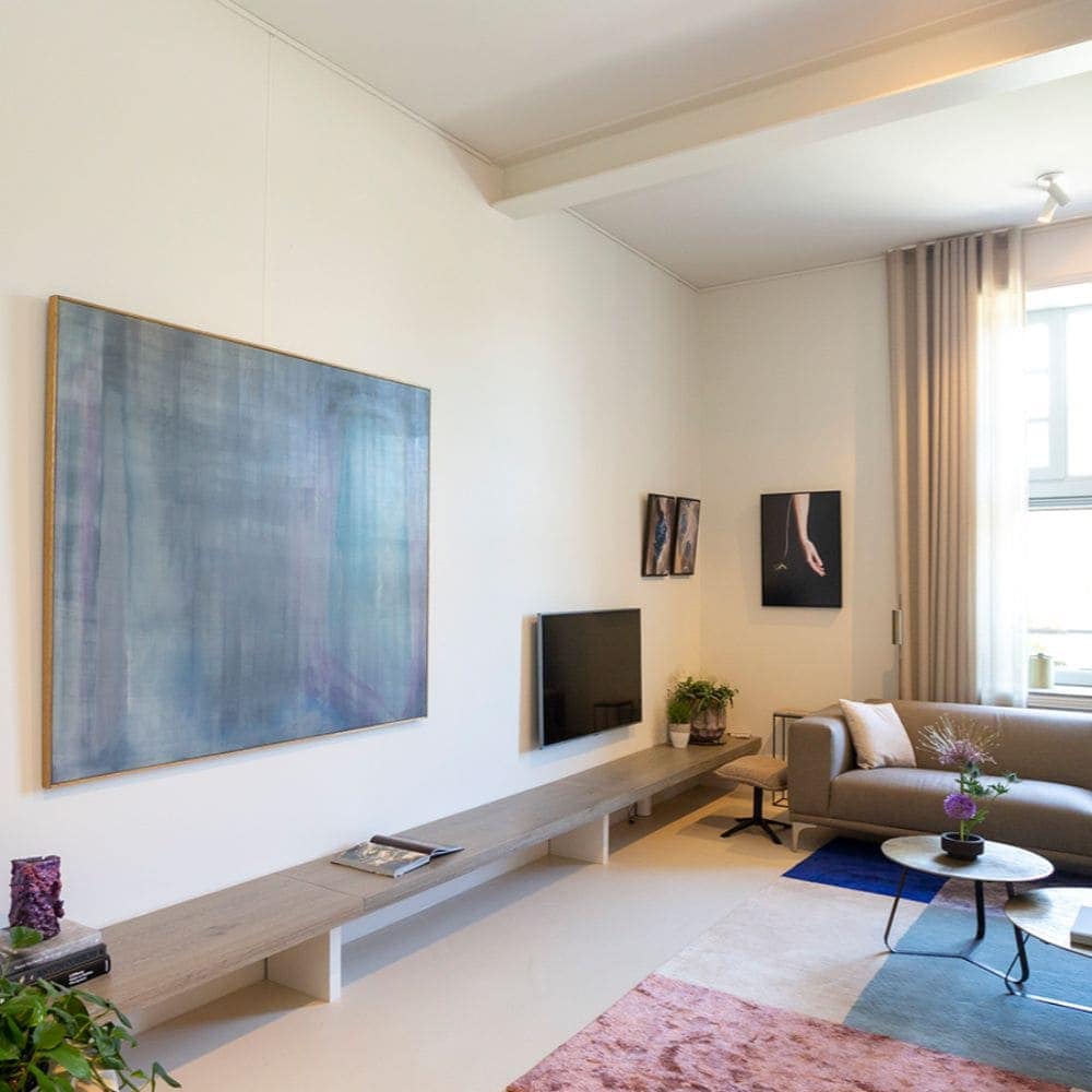 Modern living room with a large, framed artwork hanging on thin wires above a long floating shelf.