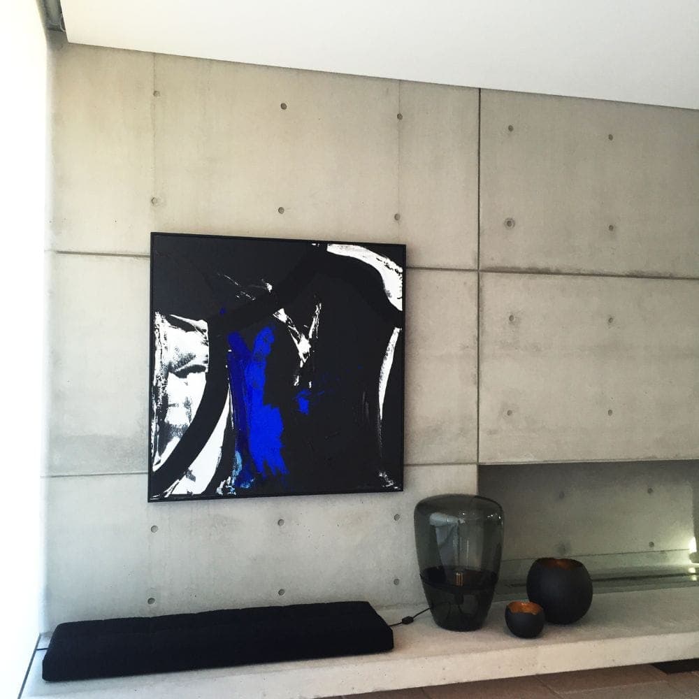 Large abstract painting hanging on a concrete wall beneath a recessed ceiling shadow line beside dark glass vessels.