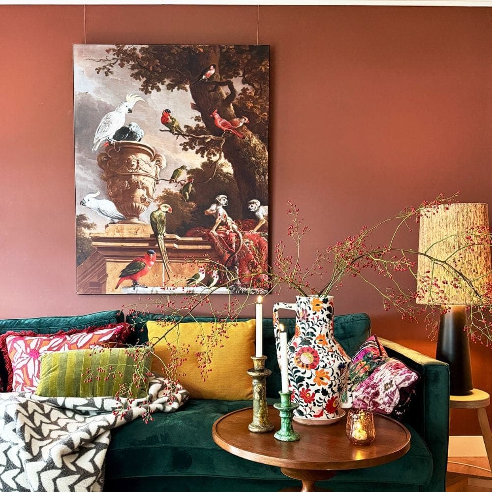 Styled living room with a large artwork suspended on fine wires above a green sofa against a warm red terracotta wall.