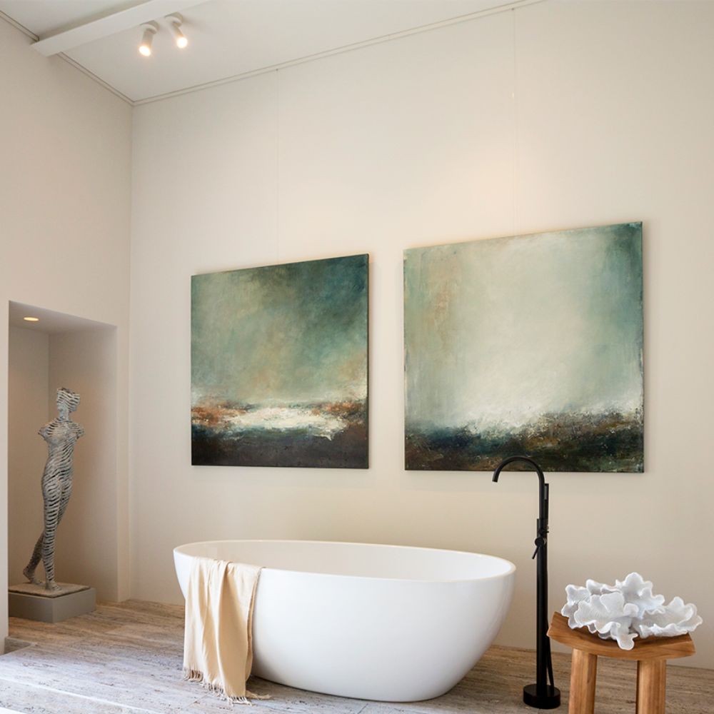 Bathroom with two large artworks suspended from fine wires below a picture rail above a freestanding bath.
